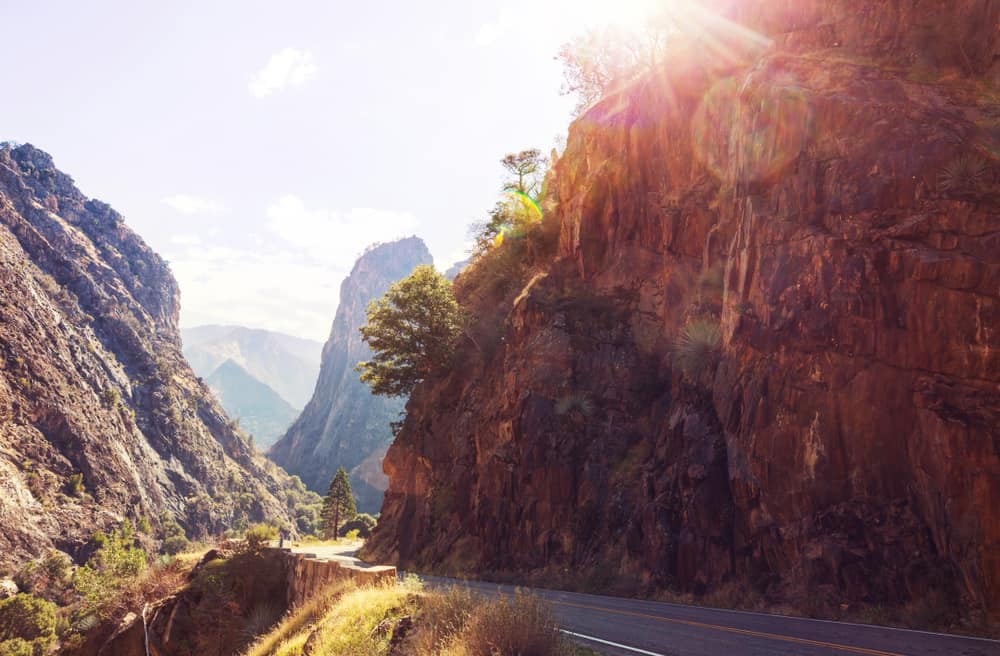 In the majestic Sequoia and Kings Canyon National Parks, the sun graciously shines down on a winding road nestled amidst towering mountains.