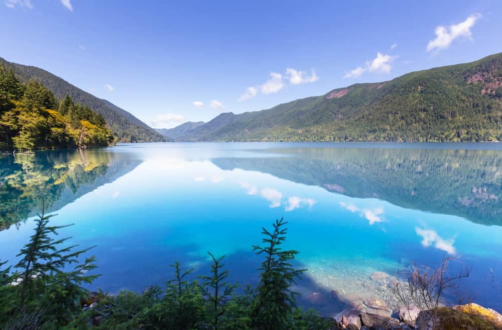 A blue lake surrounded by trees and mountains in the picturesque Washington National Parks, making it a perfect investment for nature lovers and outdoor enthusiasts.