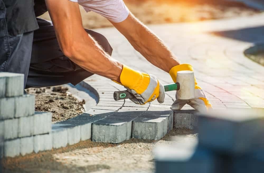 A man is laying bricks on a sidewalk as part of a repair assessment for the National Park Service's deferred maintenance.