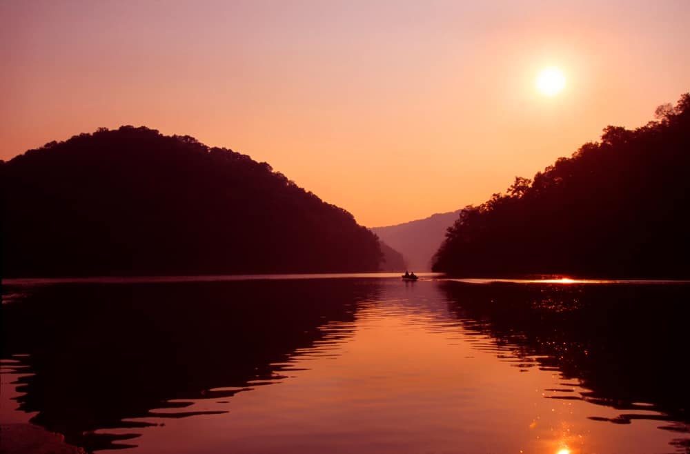 The sun is setting over a lake with mountains in the background.