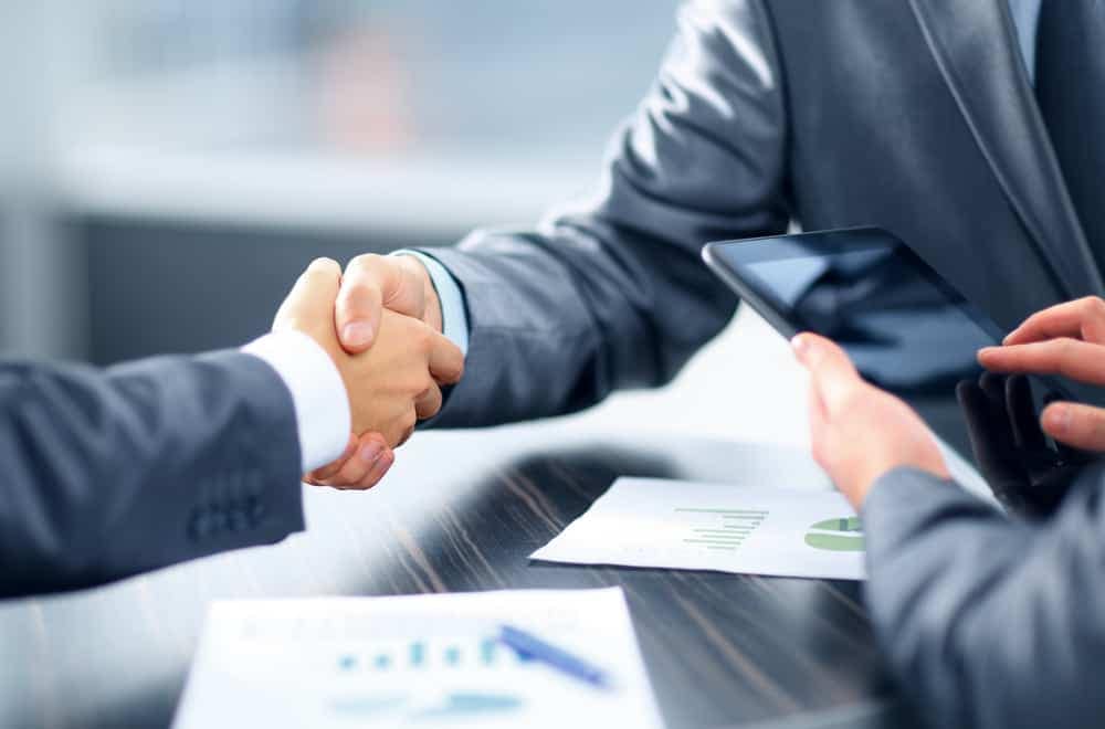 Two business people representing Pathfinder Ventures and Agassiz Expansion shaking hands at a table during a property acquisition agreement.