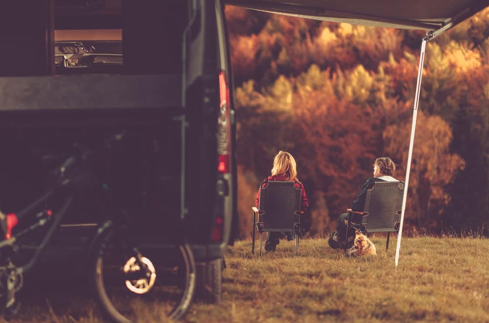 Two people sitting in front of a camper at Spacious Skies Campgrounds.
