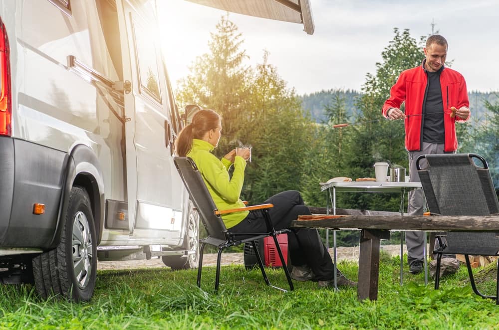A man and a woman sitting at a table near an RV, creating endless memories through RVing.