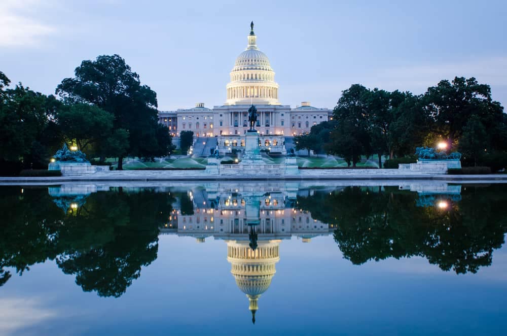The capitol building in Washington, DC is reflected in a serene pond, promoting the Outdoor Industry Association's commitment to hard work.