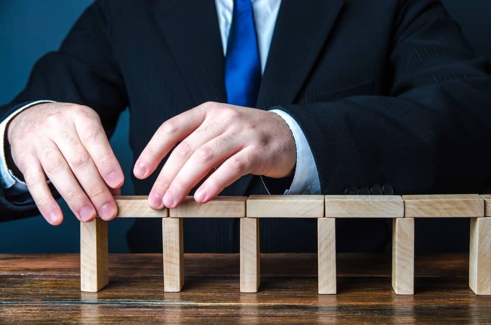 A businessman in a suit is putting together wooden blocks for local infrastructure projects.