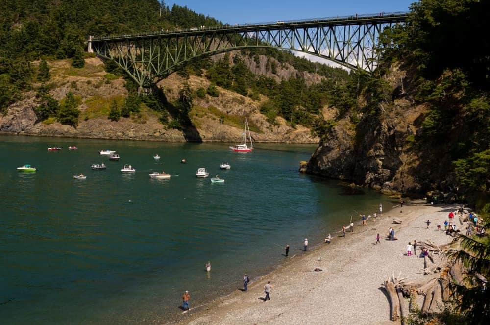 A group of people enjoying the natural beauty of Deception Pass State Park on a beach near a bridge.