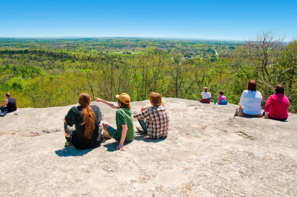 A group of campers sitting on top of a rock overlooking a forest at Maine State Park Campgrounds.