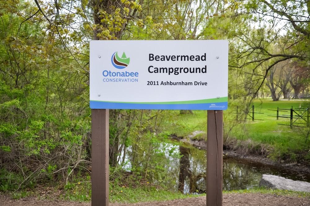 A sign that says beavermead campground in front of a pond.