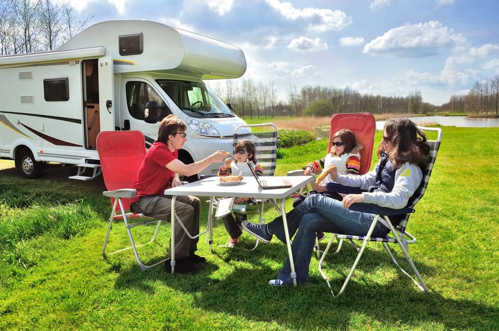 A group of people sitting at a table near an RV, discussing the forecast for RV shipments.