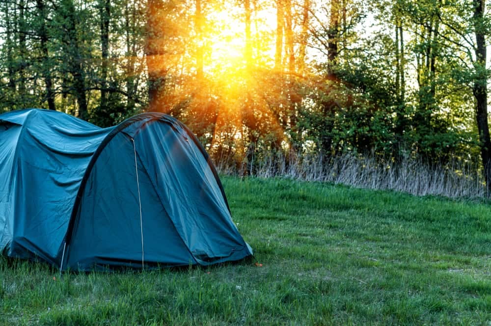 A camping tent set up in a grassy area with trees in the background.