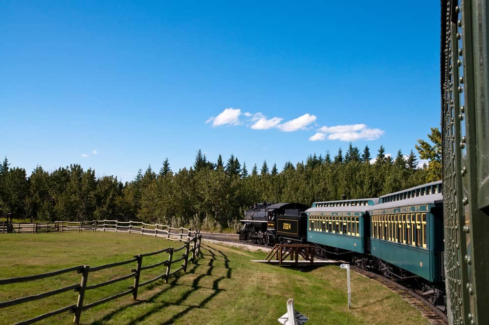 A train traveling down a track next to a fence, offering breathtaking views of the great season in Alberta.