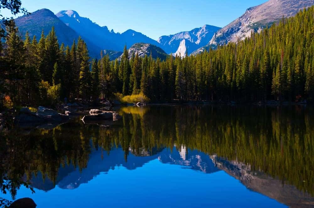 A picturesque lake nestled amidst majestic mountains and towering trees, located within the boundaries of Rocky Mountain National Park.