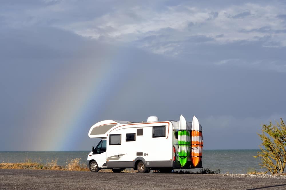 An rv with surfboards parked in front of a rainbow in Australia.