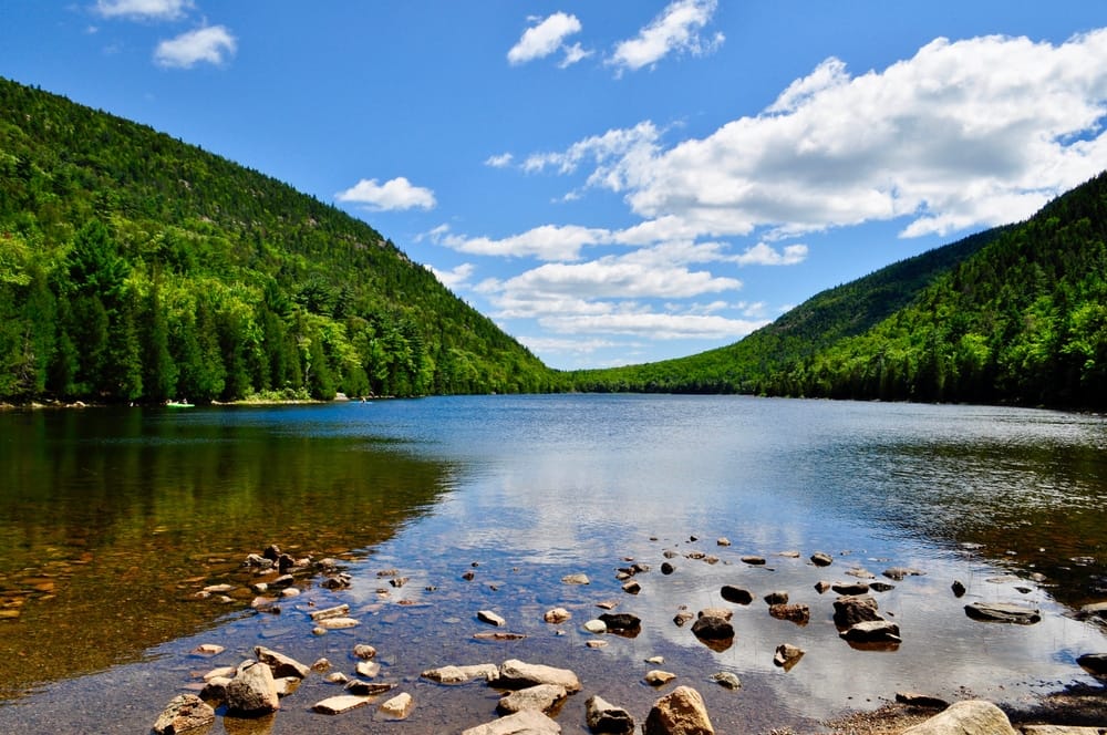 A lake surrounded by trees and rocks in Maine, where communities grapple with glamping developments.
