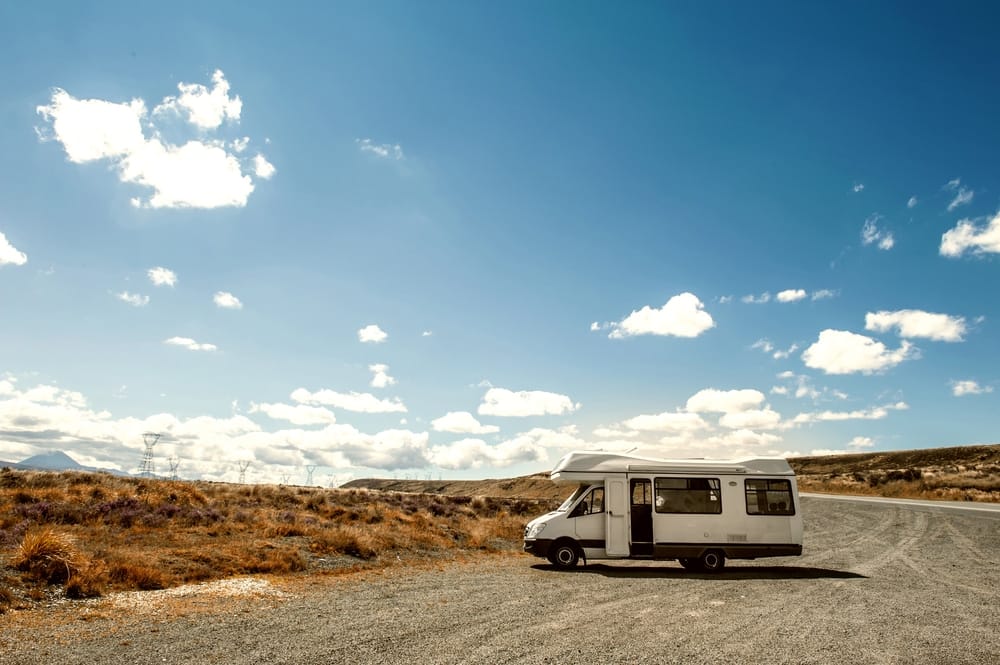 A white camper van is parked on a dirt road.