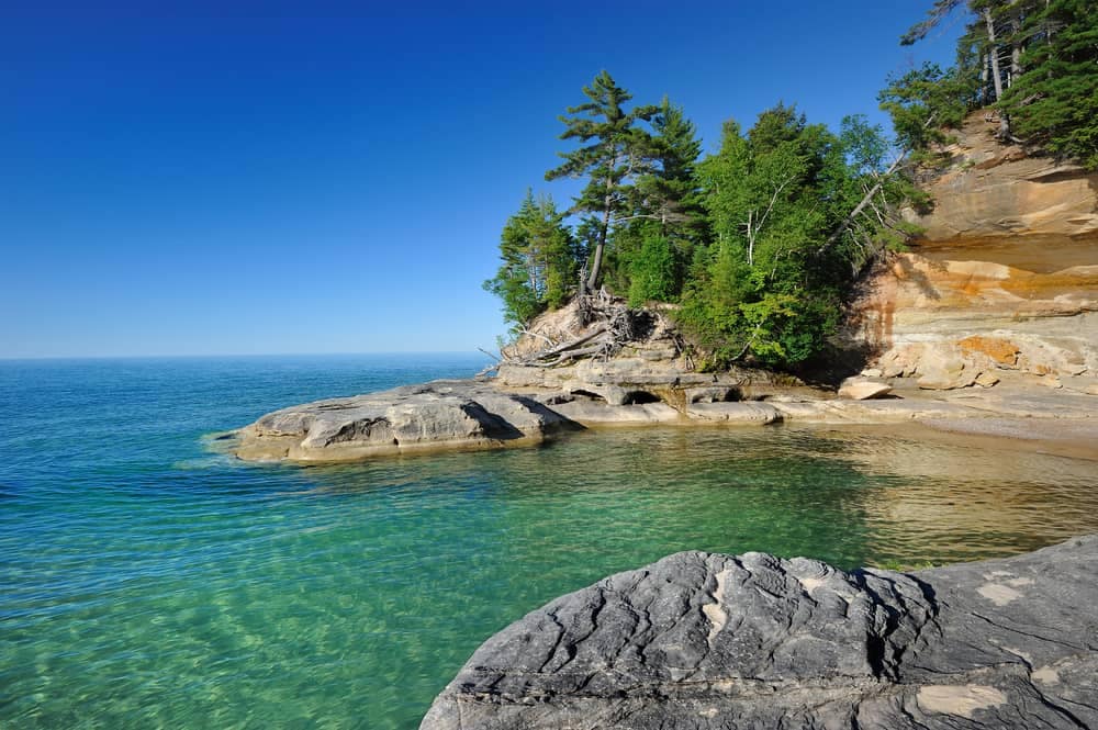 A rocky shore with clear water and trees in one of the Five Lake Superior National Parks.