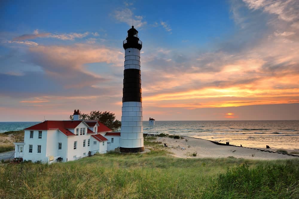 A lighthouse sits on top of a sand dune at a Michigan State Park during sunset, offering breathtaking views.