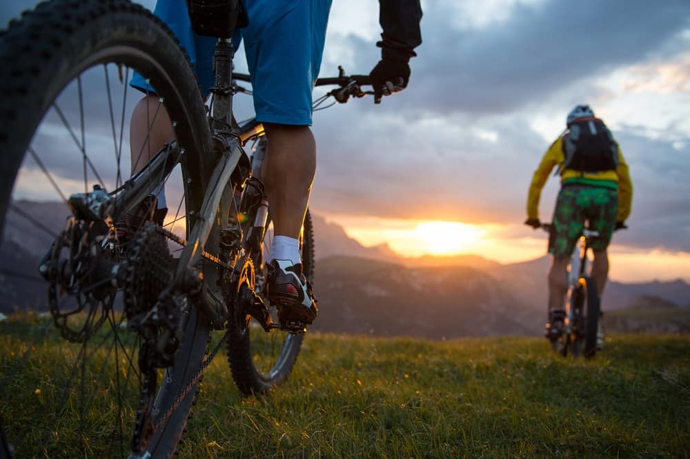 Two people enjoying outdoor adventures riding mountain bikes at sunset.