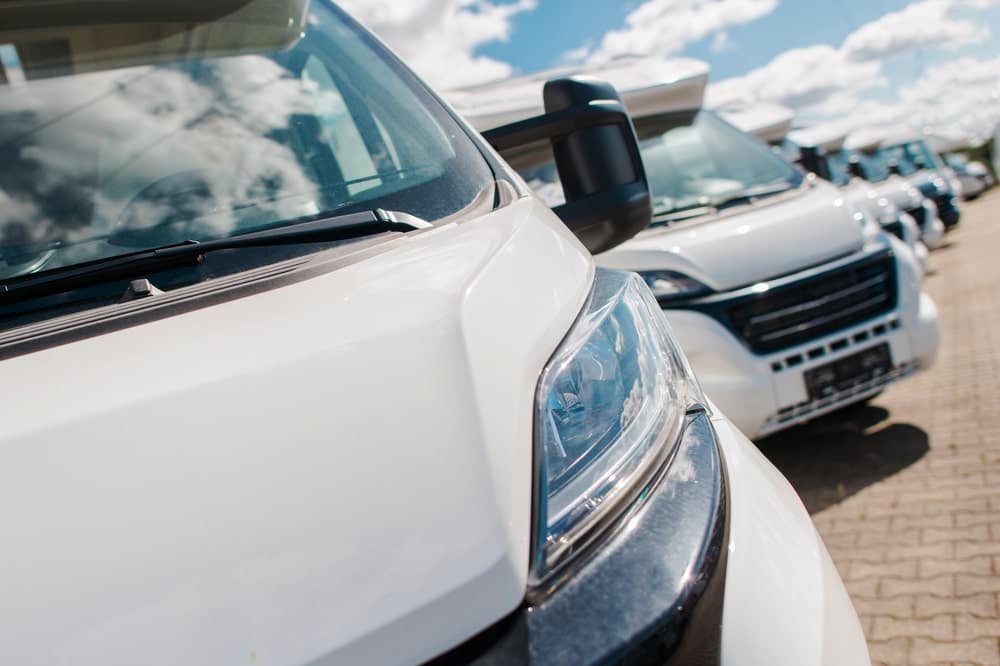 A row of white vans, commonly used by professionals in the RV industry, parked in a parking lot.
