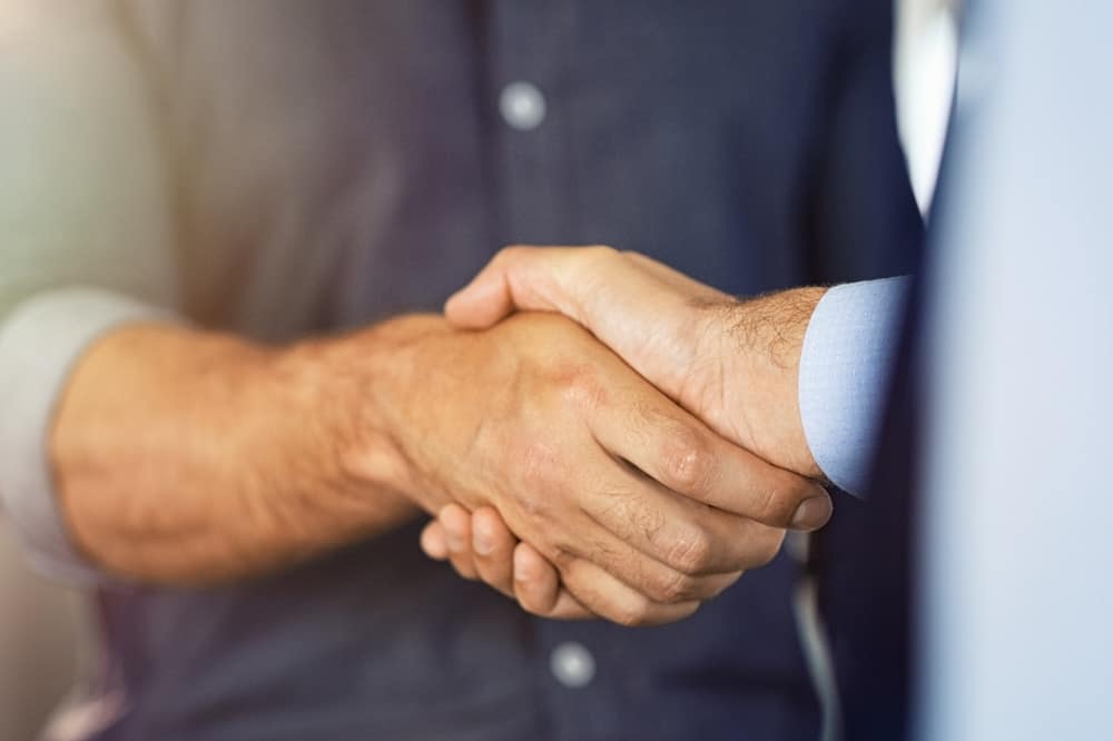 Two businessmen shaking hands in front of a Dragonfly Energy Batteries background.