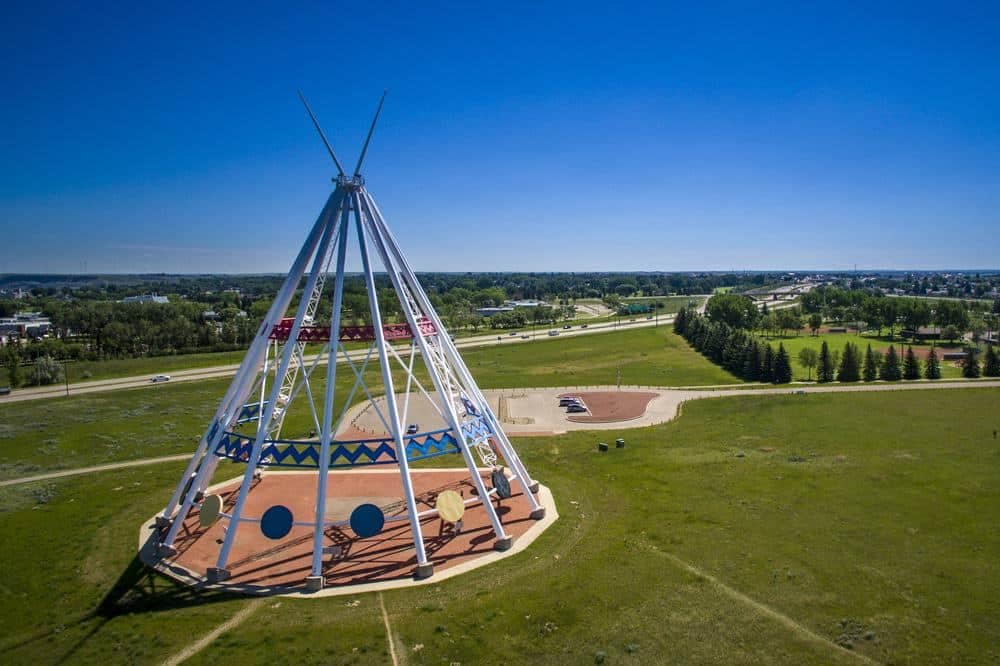 Aerial view of a teepee in the middle of a field, surrounded by serviced sites and cabins for camping.