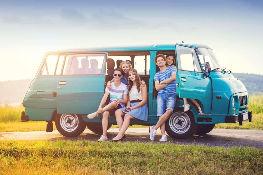 A group of young people are posing in front of a summer-ready van.