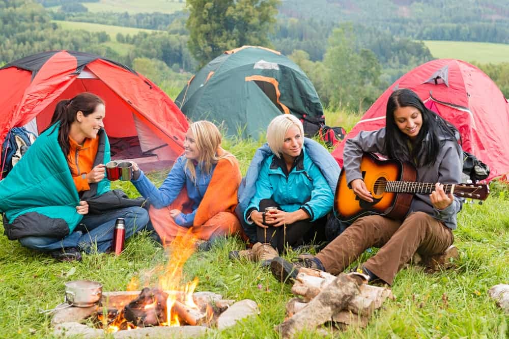 A group of women sitting around a campfire with guitars, enjoying a unique outdoor adventure.