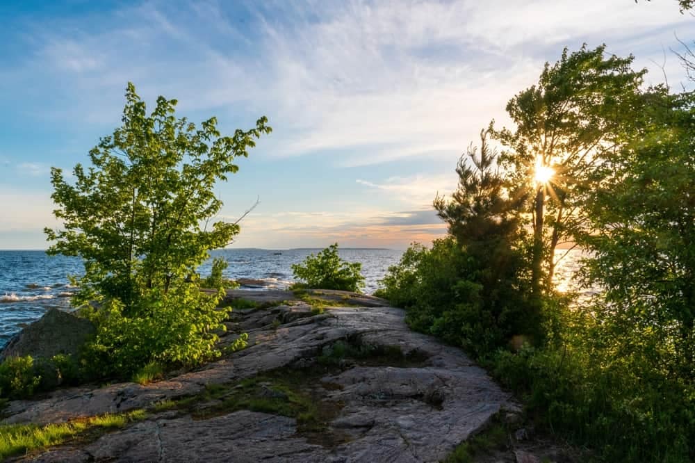 The sun is setting over the water on a rocky cliff in West Nipissing.