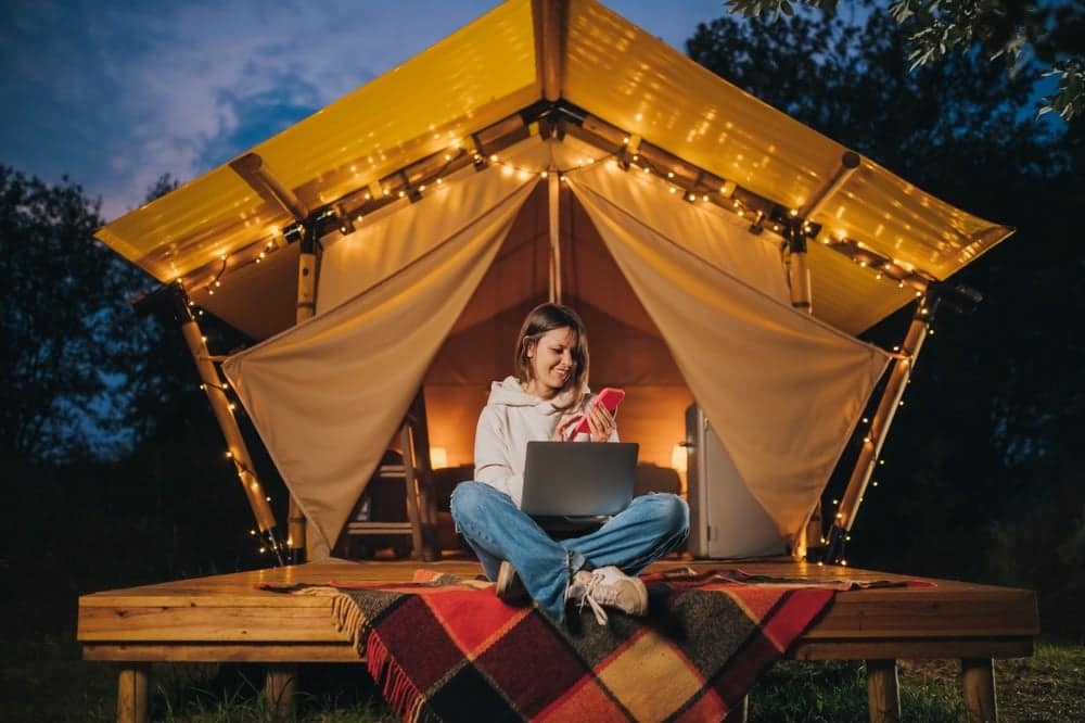 A woman sitting in front of a tent, immersed in her laptop as she enjoys an outdoor travel experience.