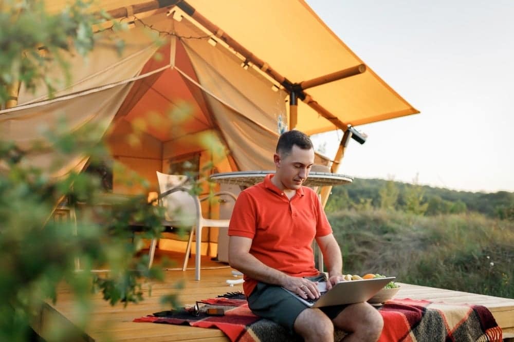 A man working on his laptop in front of a tent at a campsite in New England, gaining insights.