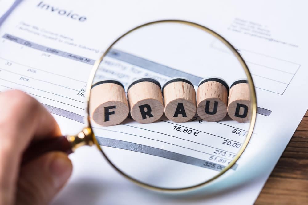 A person holding a magnifying glass with the word fraud written on it, investigating a multi-million-dollar scam.