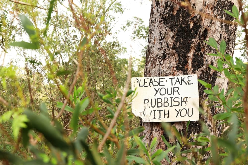 A sign on a tree that says please take your rubbish with you to discourage littering.