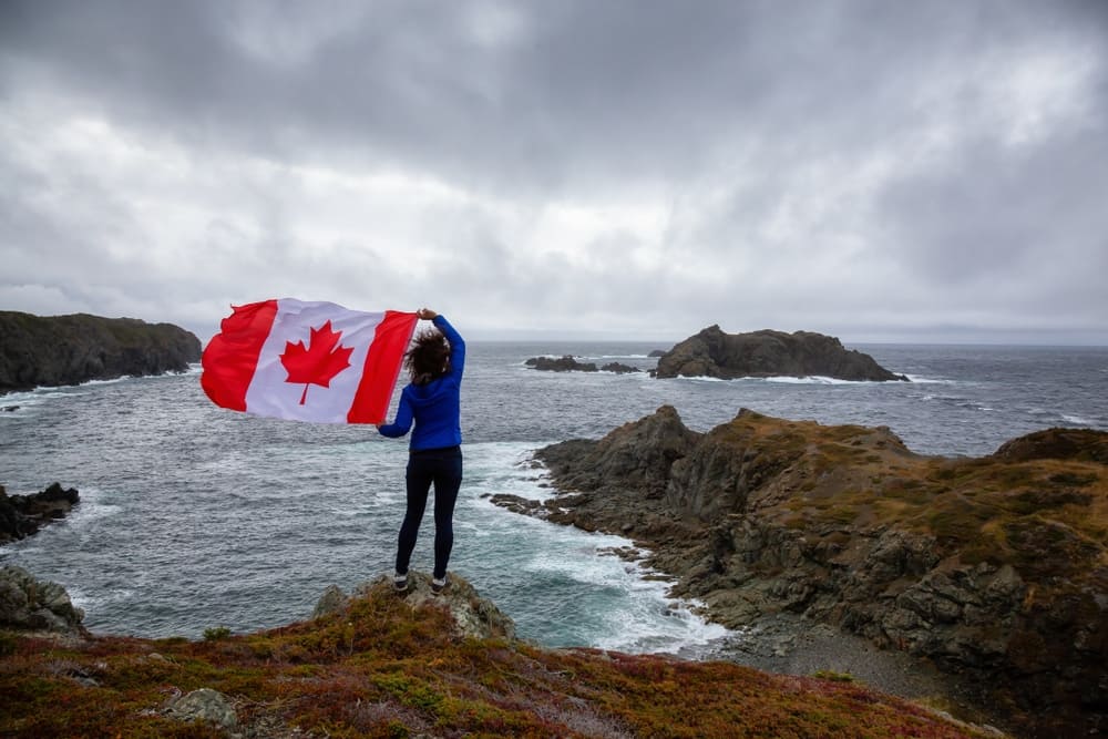 A woman holding a Canadian flag on top of a cliff, symbolizing the patriotic spirit of Canadian Snowbirds.