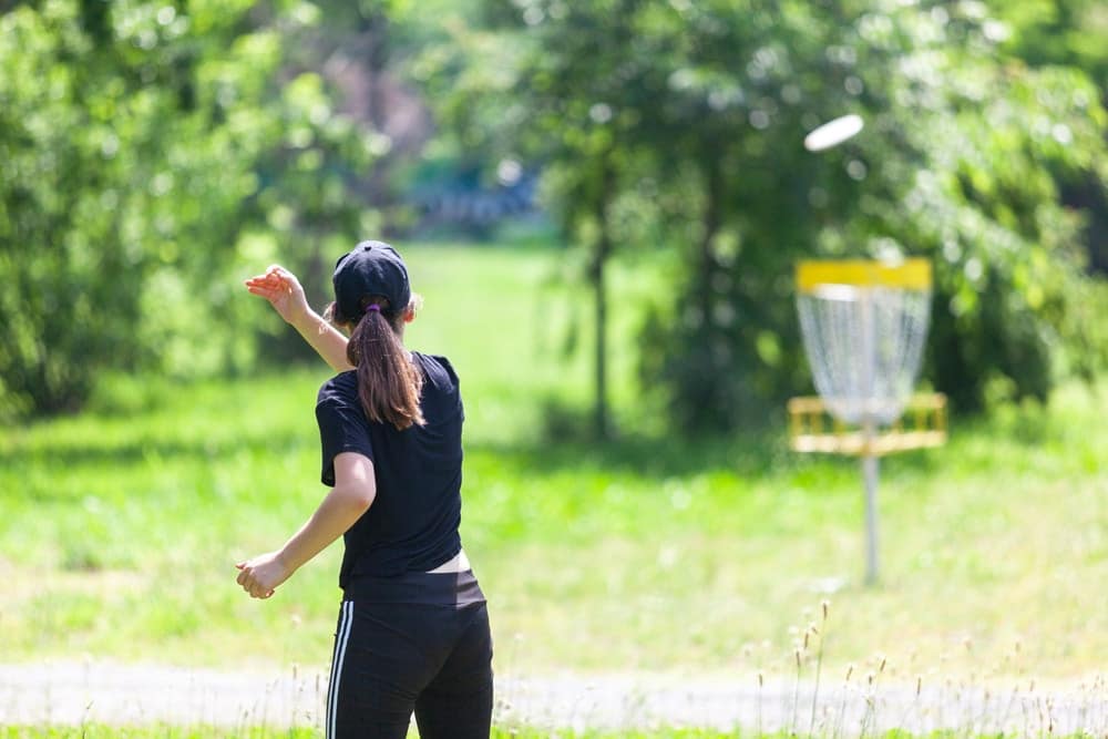 A woman is throwing a frisbee at British Columbia's Charlie Lake, a Disc Golf Course in the park.