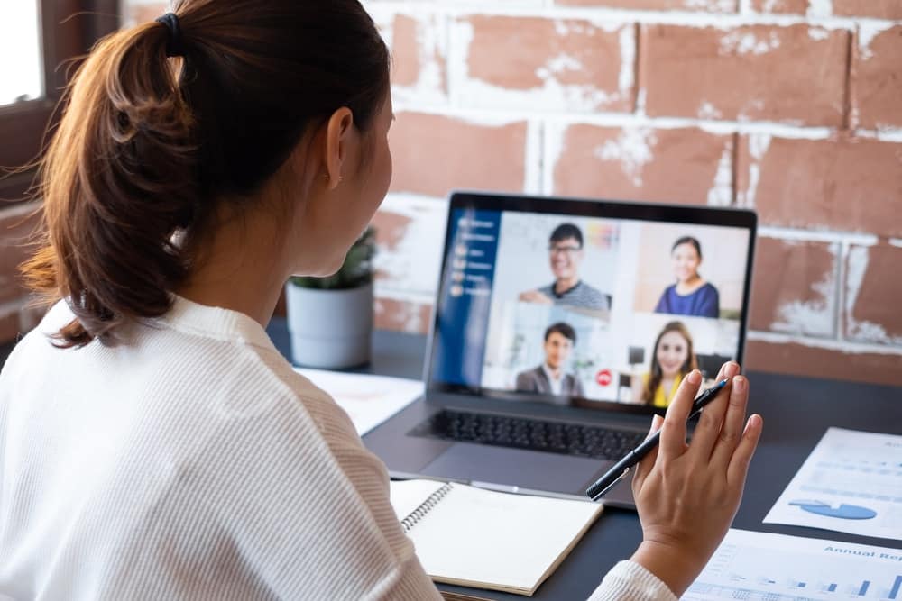 A woman is sitting at a desk with a laptop and a phone in front of her, working virtually.
