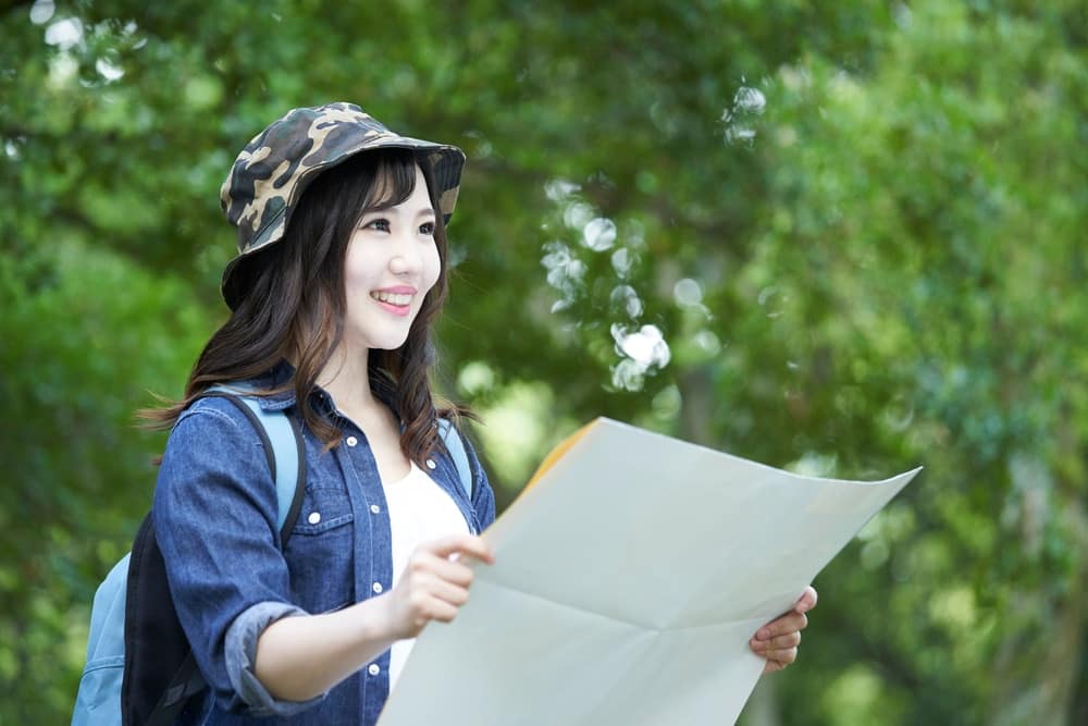 A young Japanese woman holding a map in the park.