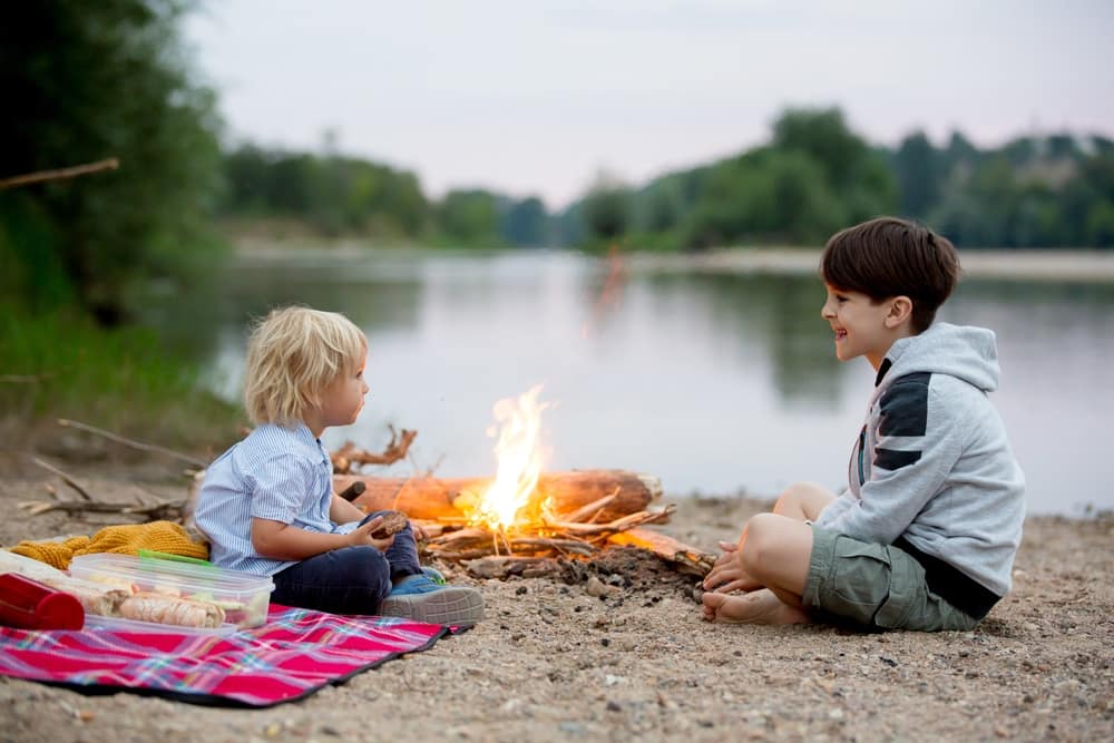 Kids sitting around a campfire near a river.