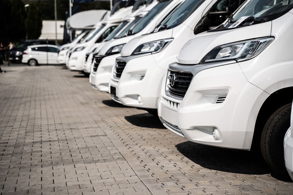 A row of white vans parked in a parking lot at a campground.