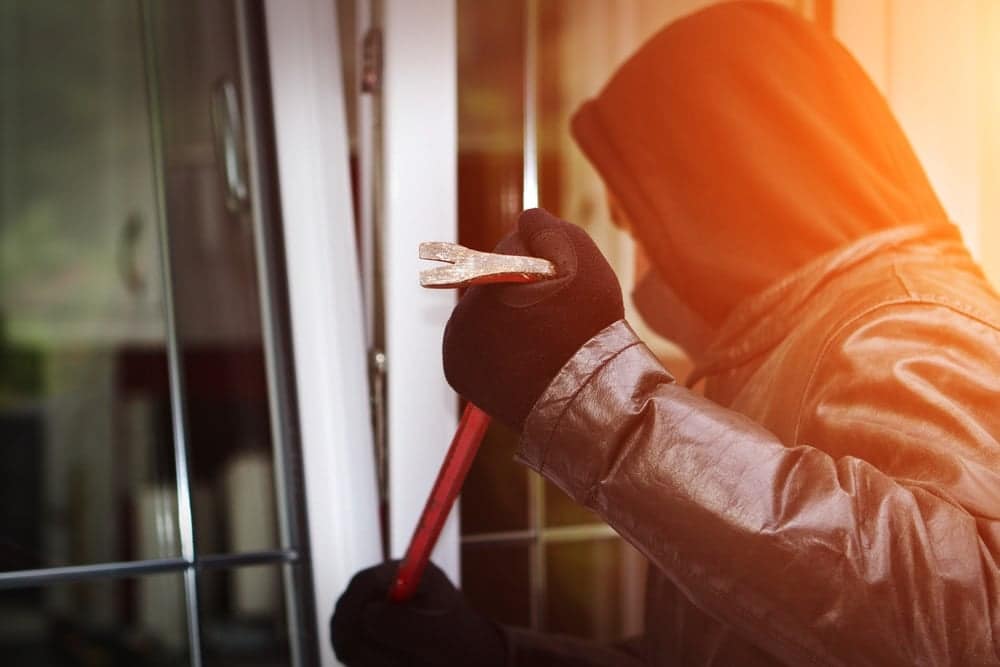 A man in a hoodie is using a hammer to open a vandalized window at an Indiana campground.