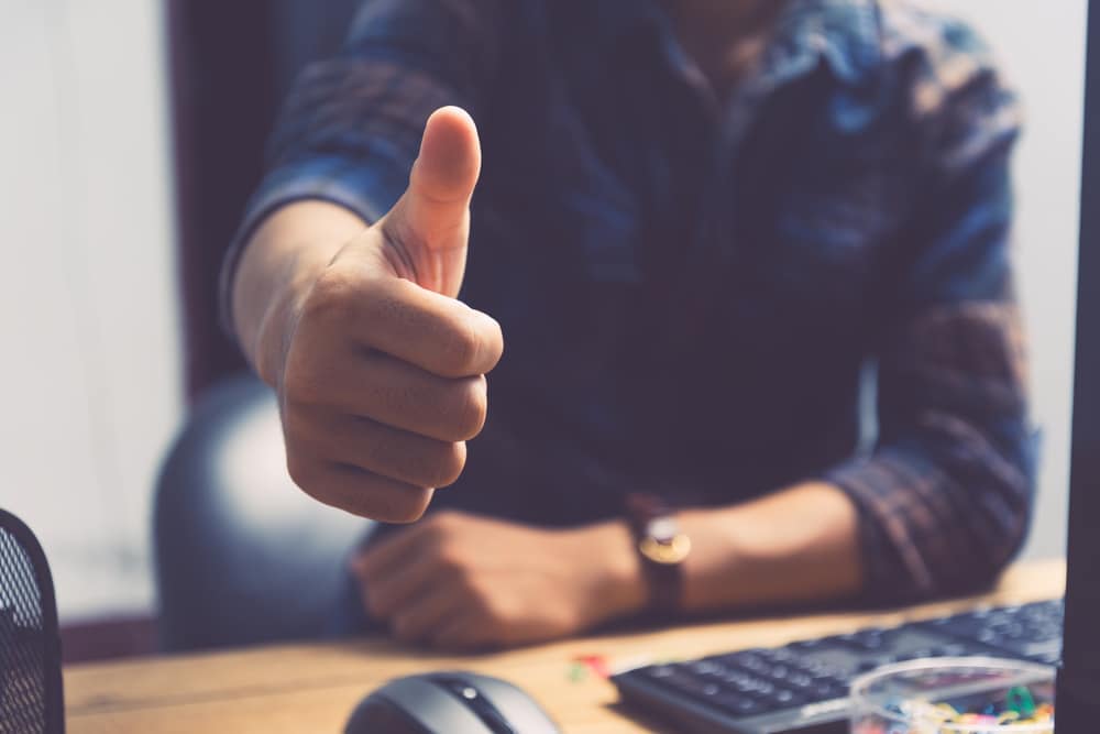 A man giving a thumbs up in front of a computer, recommended for approval.