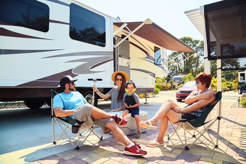 A family sits in lawn chairs in front of an rv.