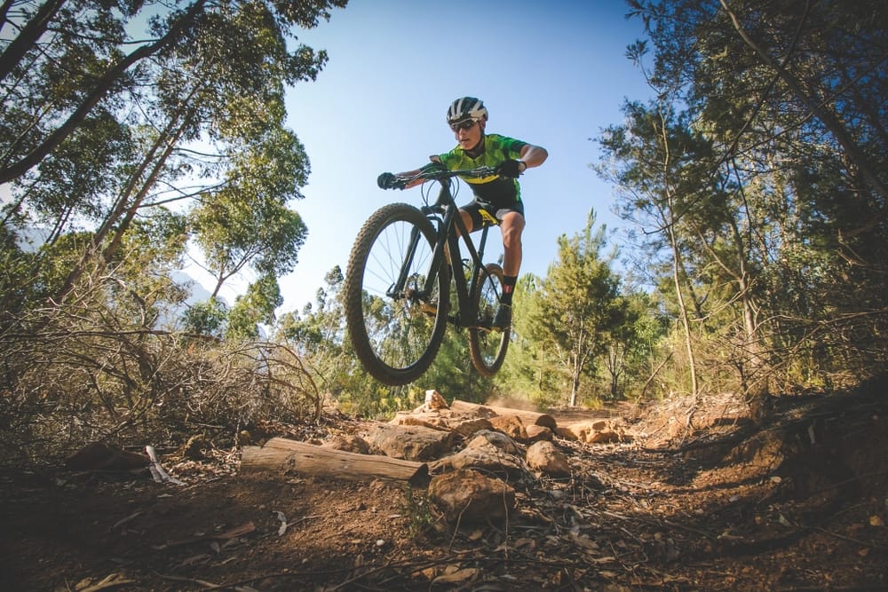 A man riding a mountain bike near the Proposed Arkansas City Campground, with Cyclists passing by and curious Neighbors observing.