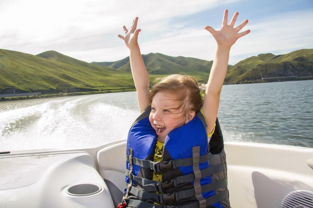 A little girl enjoying recreational boating with her arms up.