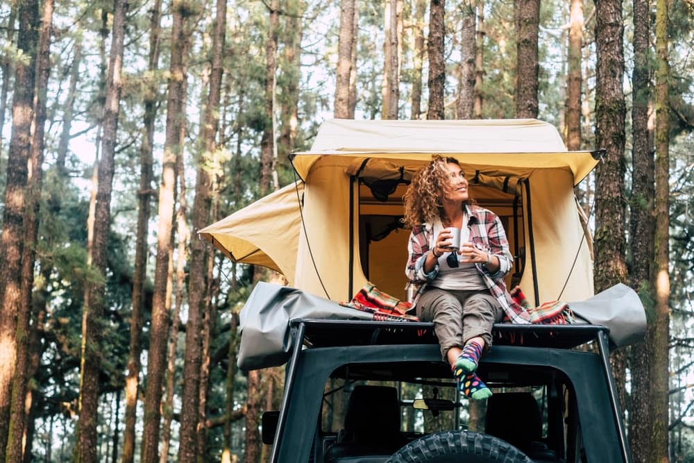 A woman sitting on top of a tent surrounded by the peaceful woods, contemplating Camplify's ASX:CHL share price.