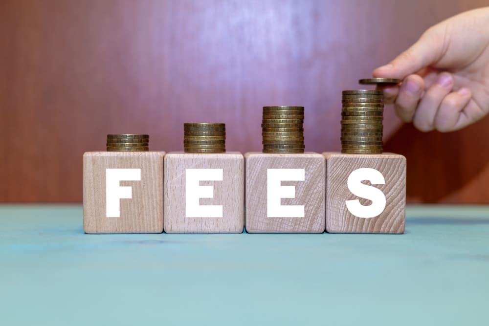 A hand is putting coins into a stack of wooden blocks that say fees.