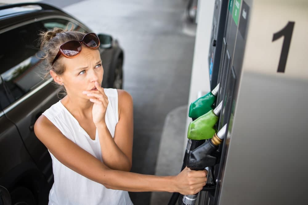A woman filling up her car at a gas station pump, confronting the ghastly gas prices that haunt consumers.