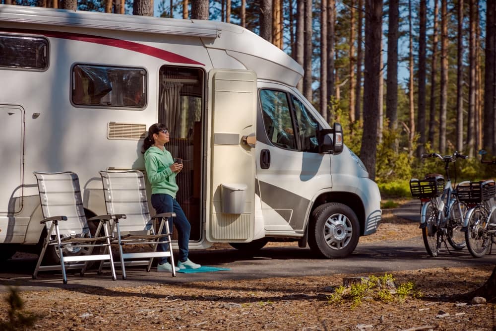 A woman standing next to an RV in the woods.