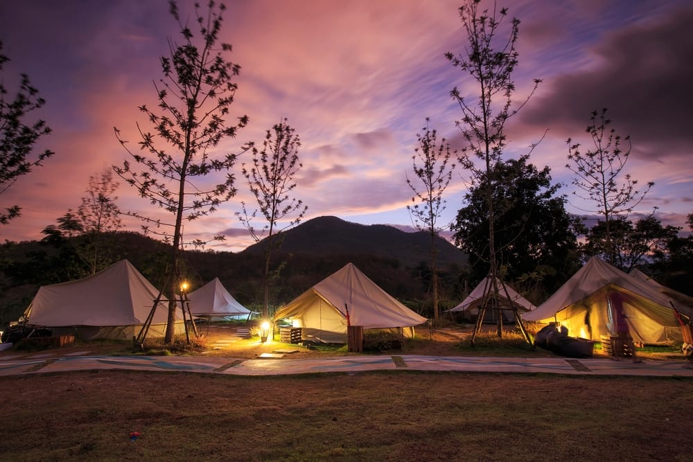 A group of tents lit up at dusk with mountains in Utah in the background.