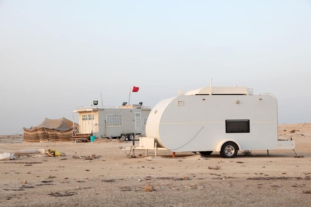 A white camper parked on the sandy beach in Qatar, providing a unique winter camping experience close to nature.