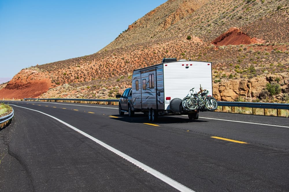 An rv traveling down a road with a bike on the back, exploring the outdoors and embracing contactless tech while enjoying a tourism adventure.